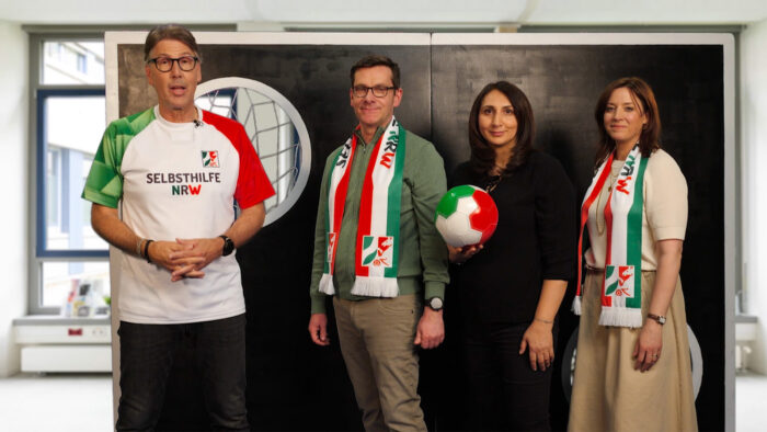 Screenshot Erklärfilm Peter Großmann, André Beermann, Öznur Naz und Kendra Zwickler posieren vor Torwand